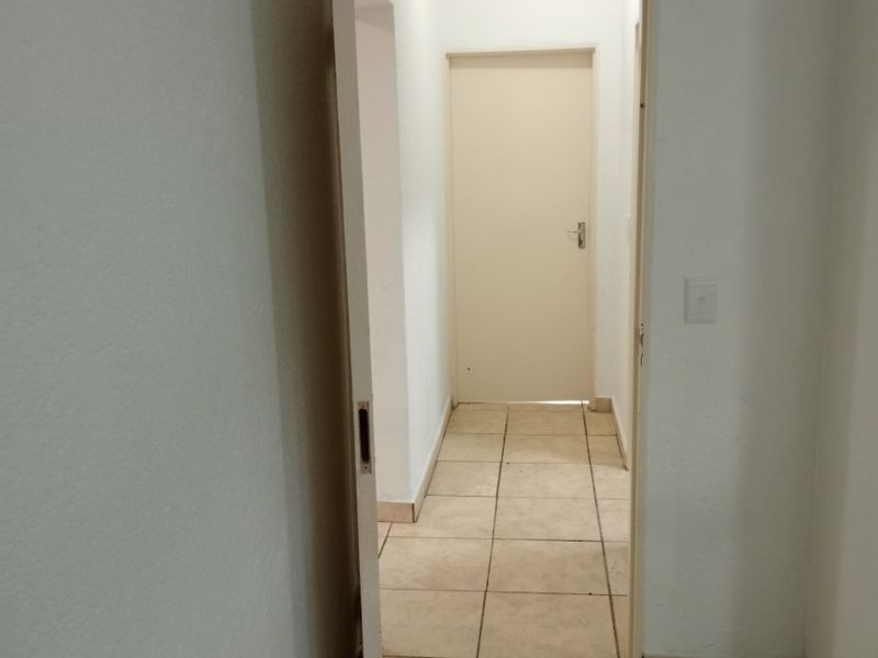 A simple interior hallway featuring neutral tiled flooring and plain white walls, connecting two separate areas of the apartment.