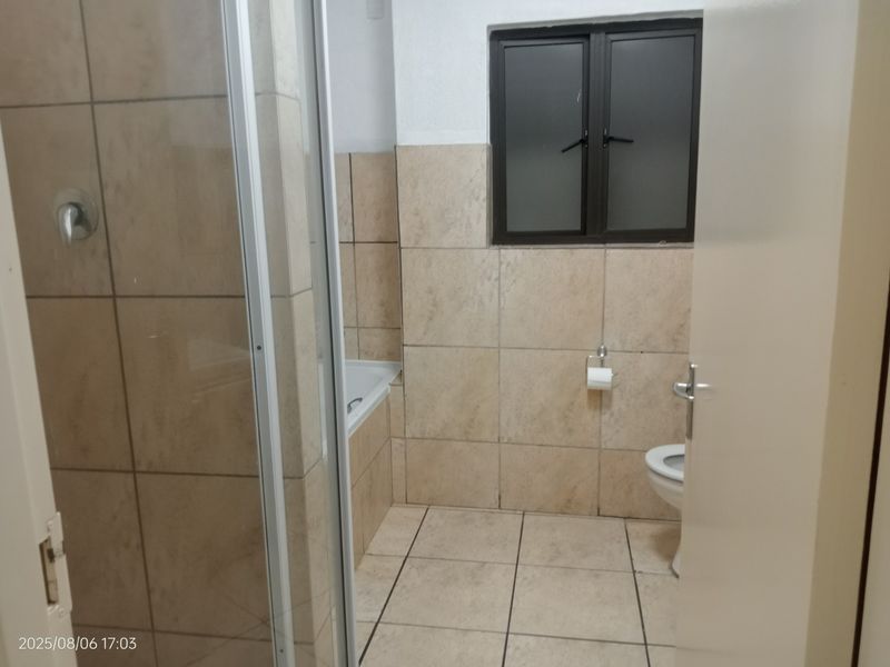 A functional bathroom featuring a shower enclosure, bathtub, toilet, and neutral tiled finishes throughout.