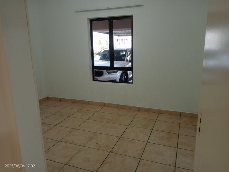 An empty bedroom featuring neutral tiled flooring and a single window with an aluminium frame, providing a blank canvas for personalization.