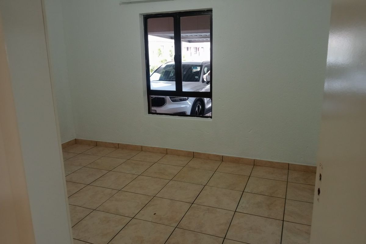 An empty bedroom featuring neutral tiled flooring and a single window with an aluminium frame, providing a blank canvas for personalization.