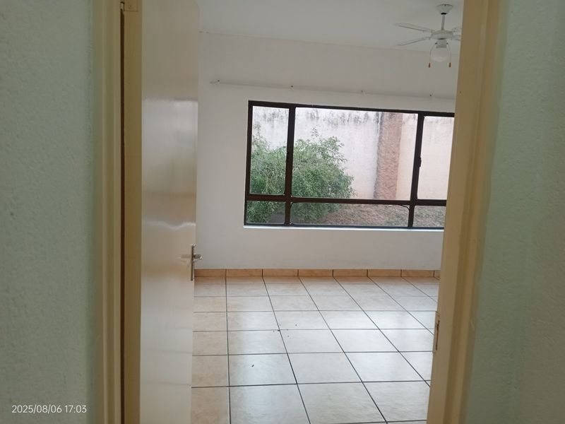 An empty bedroom featuring tiled flooring, a ceiling fan, and a large window overlooking an exterior boundary wall.