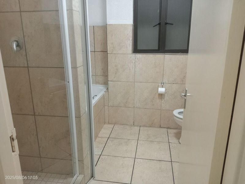 A functional bathroom featuring a shower enclosure, bathtub, toilet, and neutral floor-to-ceiling tiling.