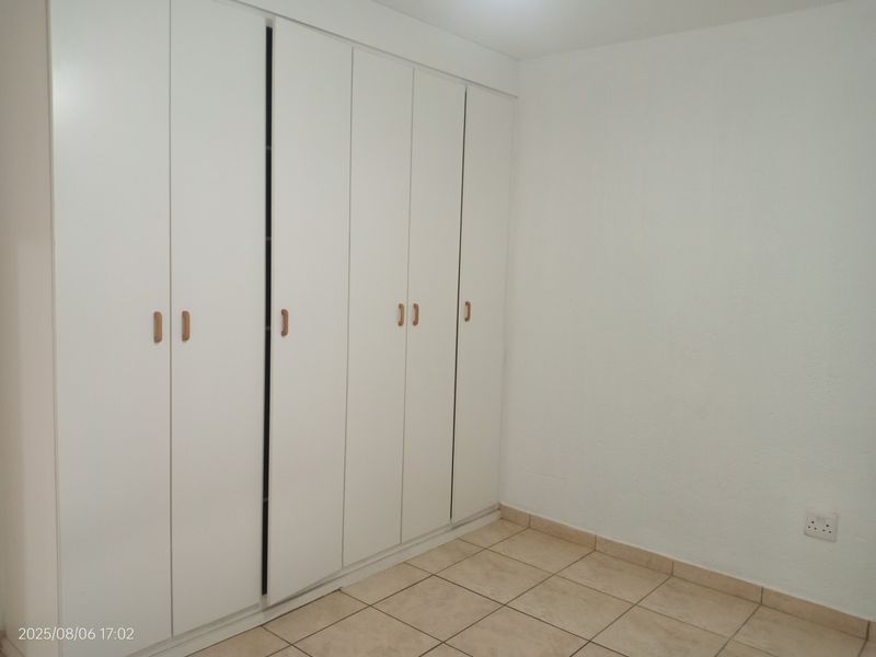 A clean, empty bedroom featuring neutral tiled flooring and extensive white built-in cupboards providing ample storage space.
