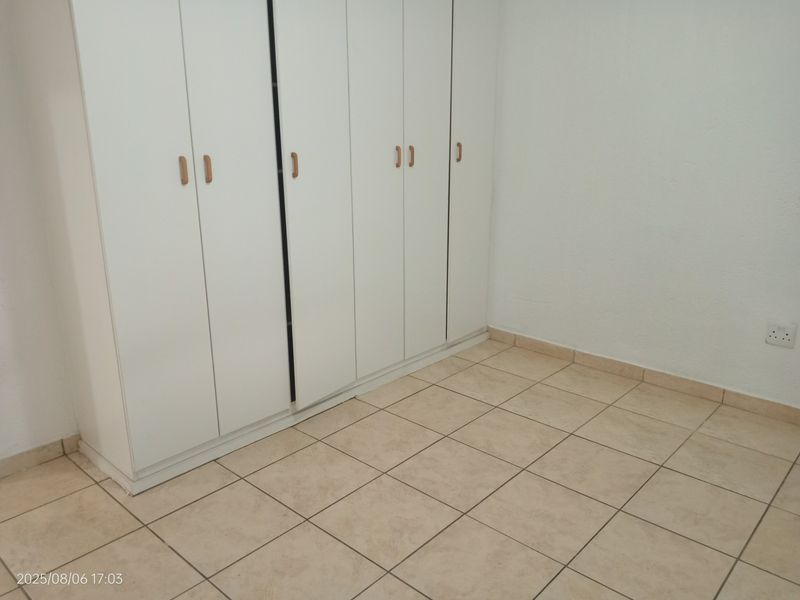 A clean, empty bedroom featuring neutral ceramic floor tiles and ample built-in cupboard storage space.