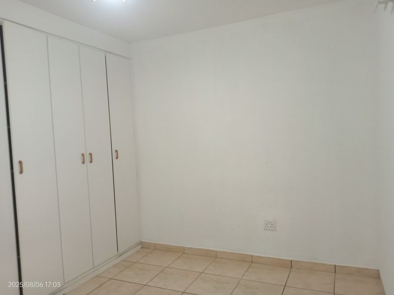 A clean, empty bedroom featuring neutral tiled flooring and white built-in cupboards, providing a blank canvas for personalization.
