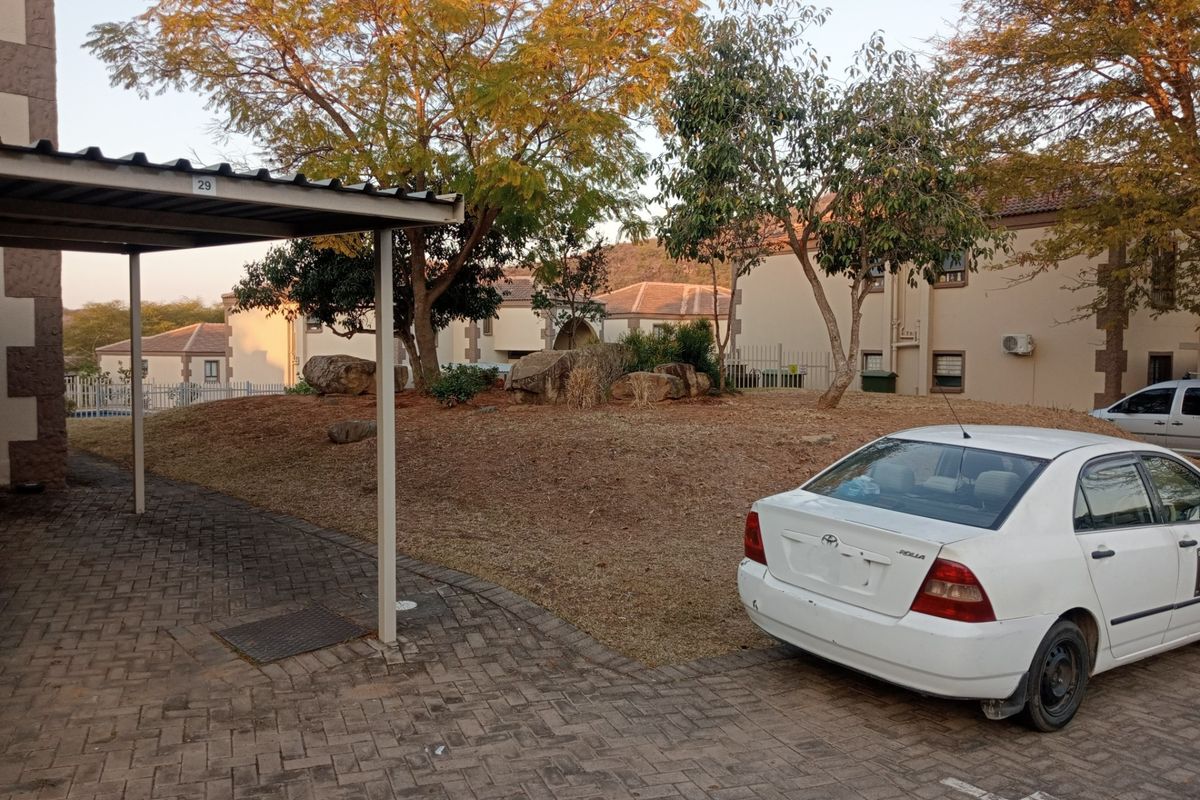 Exterior view of the apartment complex featuring a covered carport, paved driveway, and established garden area with mature trees.