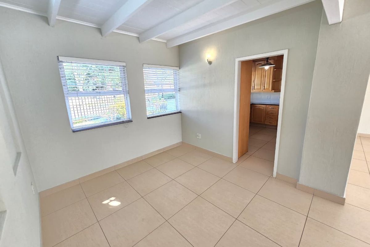 A bright, empty living area featuring tiled flooring, exposed beam ceilings, and a direct view into the adjacent kitchen.