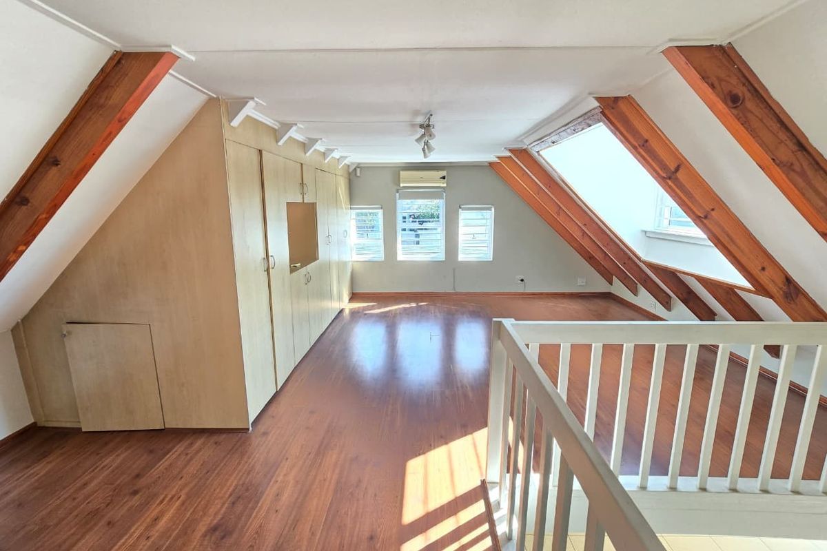 Spacious attic-style bedroom featuring exposed timber rafters, built-in cabinetry, laminate flooring, and a split-system air conditioning unit.