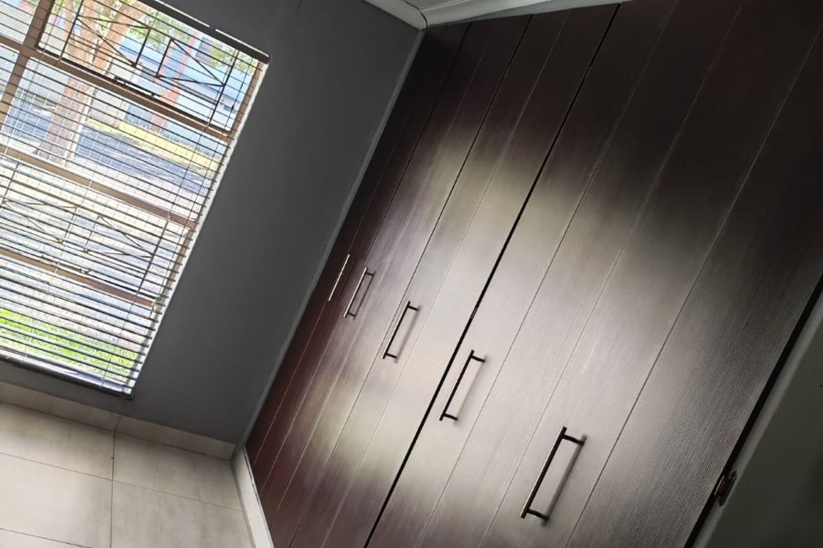 A bedroom featuring dark wood built-in cupboards, tiled flooring, and a window with security bars.