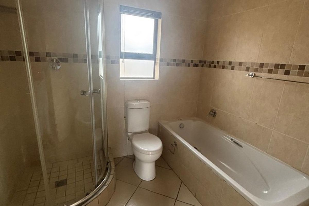 A functional bathroom featuring a corner glass shower enclosure, a built-in bathtub, and a standard toilet with neutral wall and floor tiling.