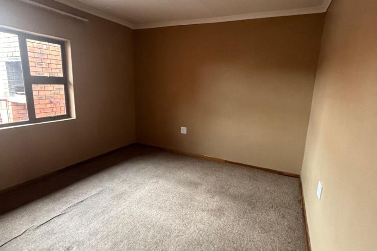 An empty bedroom featuring neutral wall tones, a single window, and fitted carpeting, providing a blank canvas for personalization.