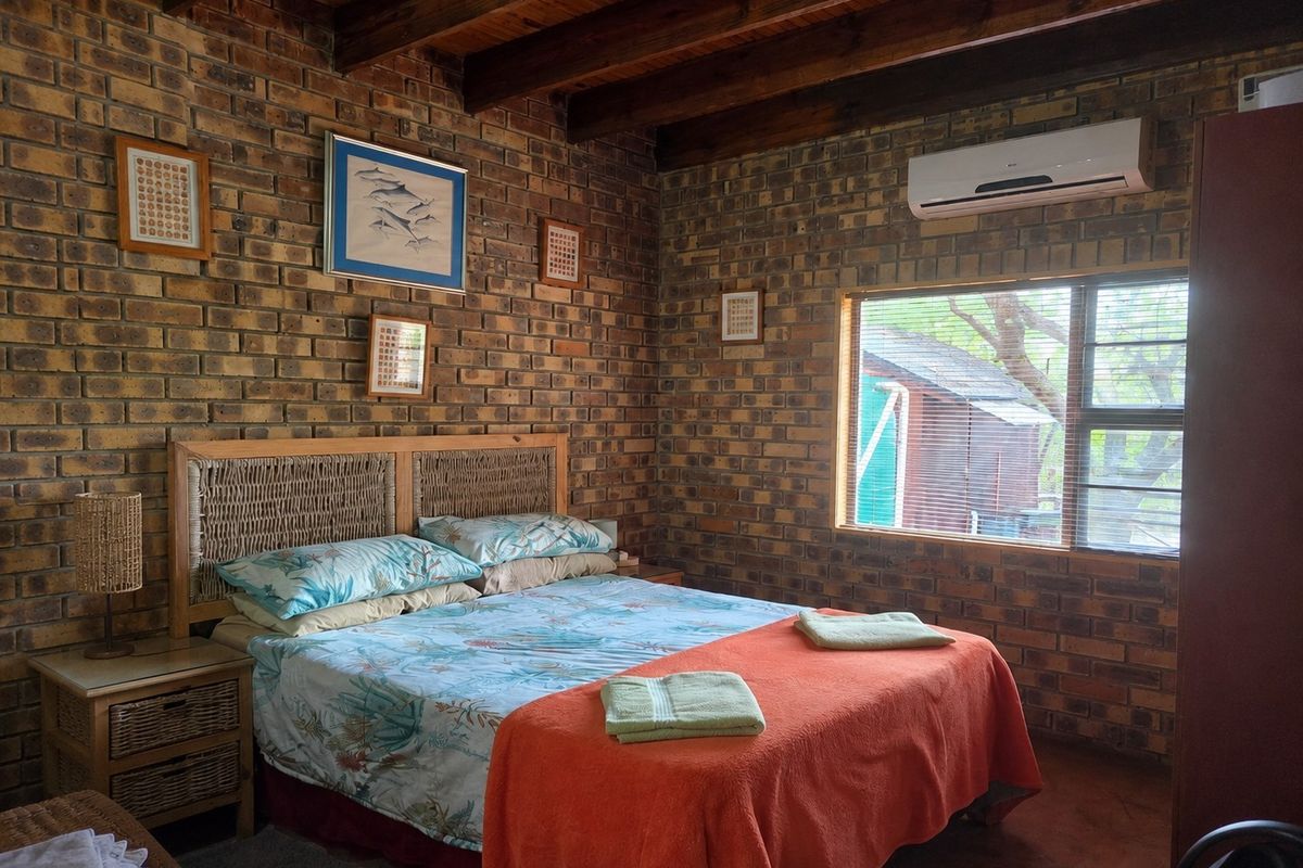 A rustic bedroom featuring exposed face-brick walls, timber beam ceilings, and a wall-mounted air conditioning unit.