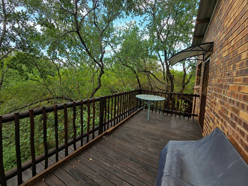 A wooden balcony deck featuring a rustic timber railing, overlooking lush surrounding trees and greenery.