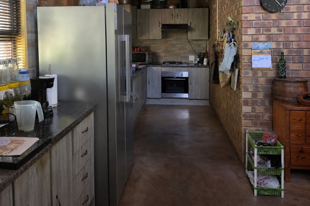 A functional kitchen featuring exposed brick walls, concrete flooring, wood-look cabinetry, a built-in oven, gas hob, and an extractor fan.