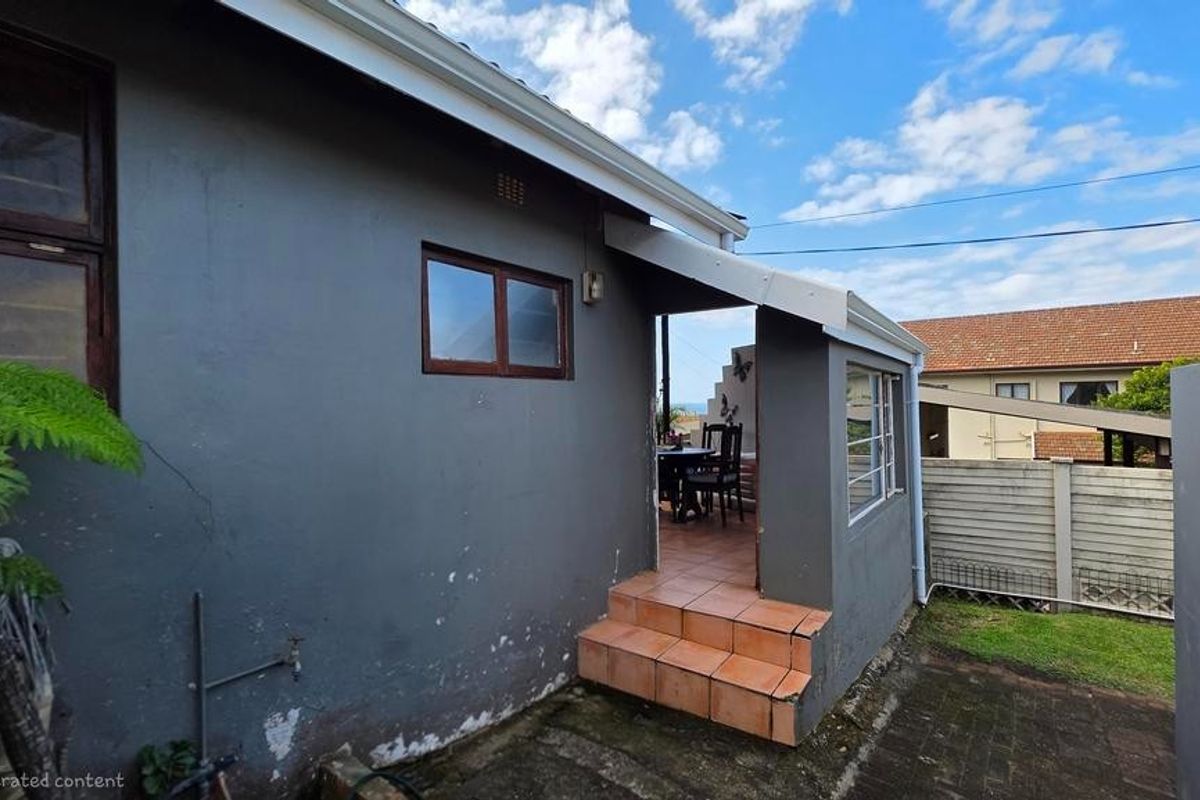 Exterior view of the rear of the house featuring a tiled patio entrance, dark grey painted walls, and paved ground area.