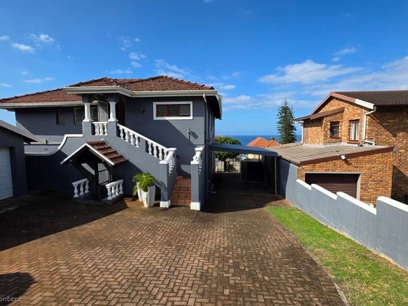Exterior view of a multi-level residential property featuring a paved driveway, covered carport, and a staircase leading to the upper level entrance.