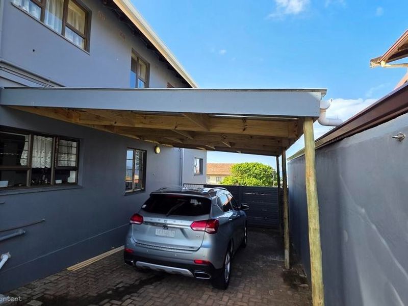 A covered carport area featuring a timber-framed roof structure, paved driveway, and direct access to the side of the house.