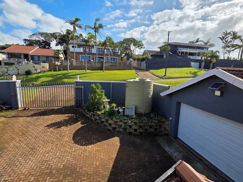 Exterior view of the property driveway featuring a garage, metal security gate, and a water storage tank set against a landscaped garden.