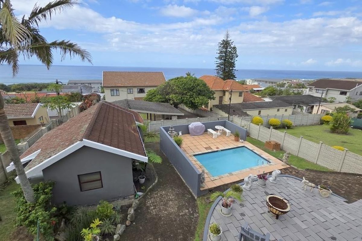 Aerial view of a residential property featuring a swimming pool, paved patio area, and a detached outbuilding, set against a coastal backdrop.
