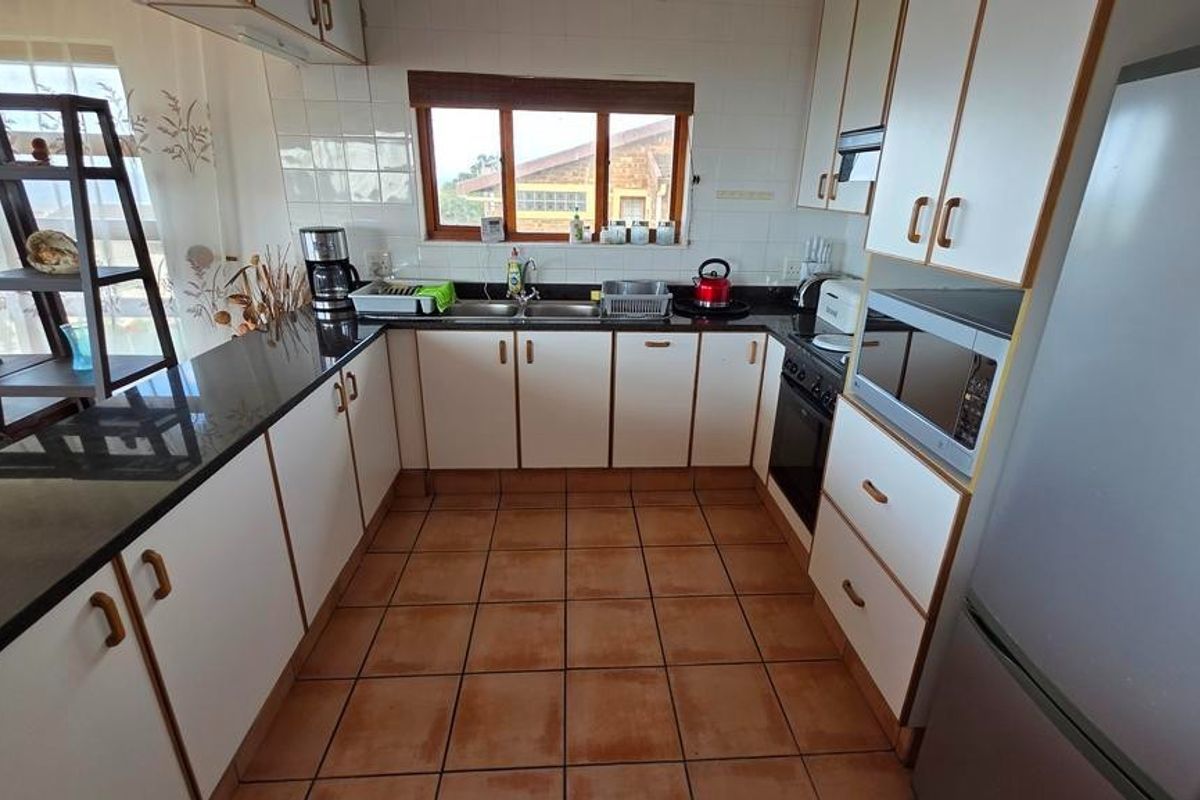 A functional kitchen featuring white cabinetry, dark countertops, tiled flooring, and a built-in oven with an extractor fan.