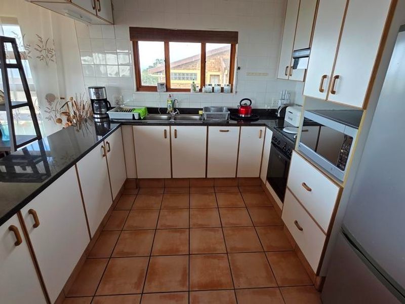 A functional kitchen featuring white cabinetry, dark countertops, tiled flooring, and a built-in oven with an extractor fan.