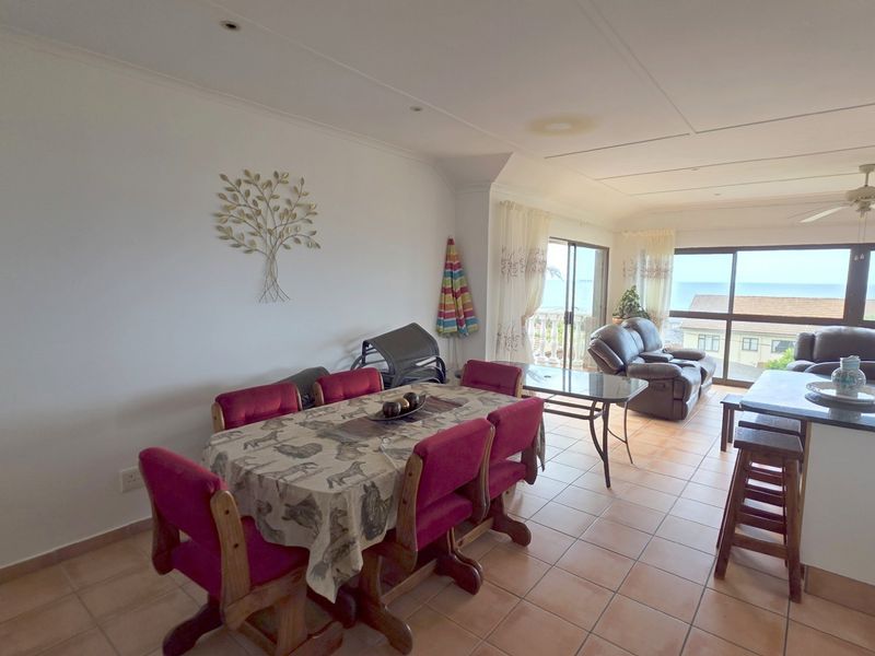 Open-plan living and dining area featuring tiled flooring, recessed lighting, and large sliding doors leading to a balcony with ocean views.