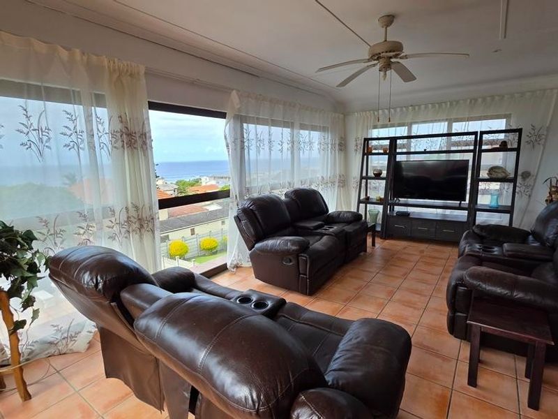 Spacious living area featuring large windows with ocean views, tiled flooring, and a ceiling fan, seamlessly connected to the kitchen area.