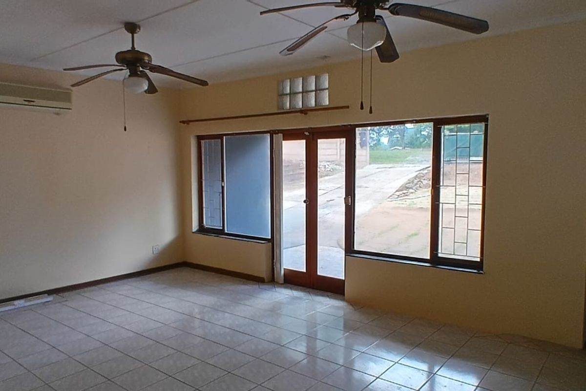 Spacious living area featuring tiled flooring, dual ceiling fans, wall-mounted air conditioning unit, and direct access to the exterior through glass-paneled doors.