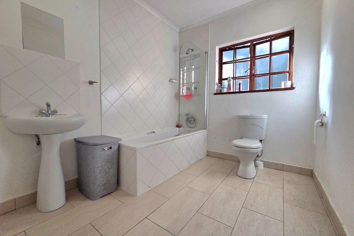 A functional bathroom featuring a pedestal basin, a bathtub with a glass shower screen, and a toilet, finished with neutral floor and wall tiling.