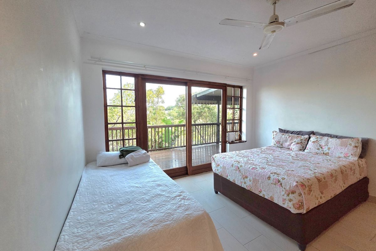 Spacious bedroom featuring tiled flooring, a ceiling fan, and large wooden sliding doors that open onto a private balcony with scenic views.