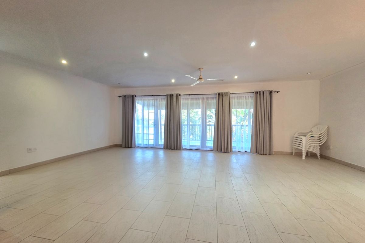 Spacious open-plan living area featuring light-toned floor tiles, recessed ceiling lighting, a central ceiling fan, and large glass doors leading to an outdoor space.