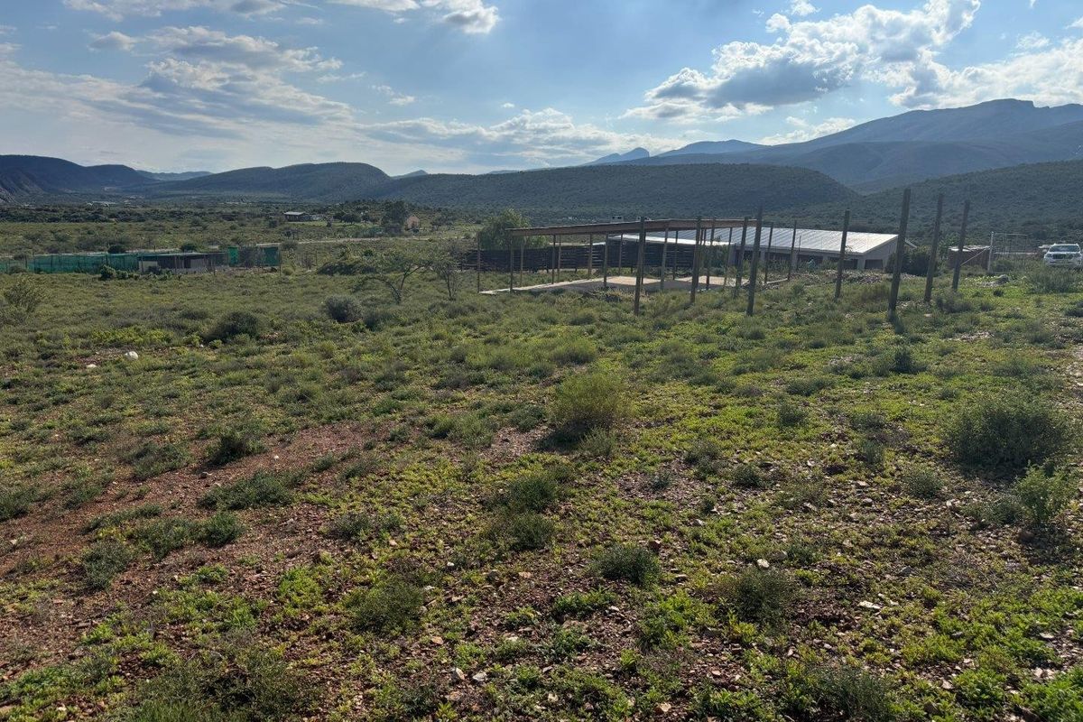 Expansive farm land featuring an unfinished timber-framed structure set against a scenic mountain backdrop.
