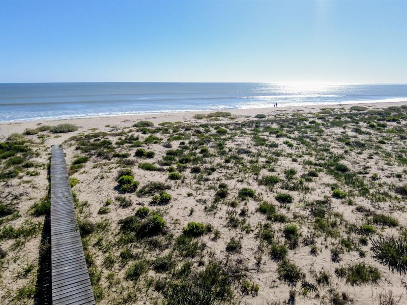 Scenic elevated view of the coastal dunes and sandy beach with a direct wooden boardwalk access path to the ocean.