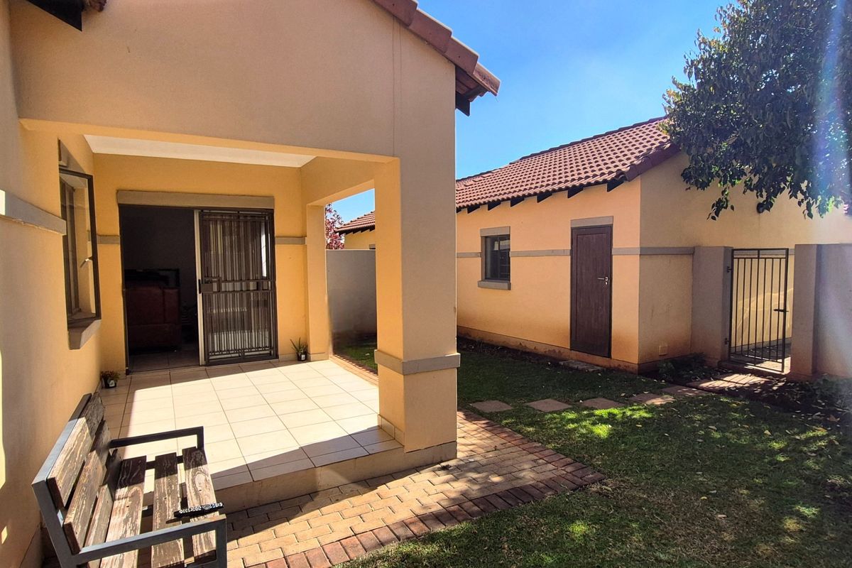 Rear view of the townhouse featuring a covered tiled patio, paved garden walkway, and secure access points to the main living area.