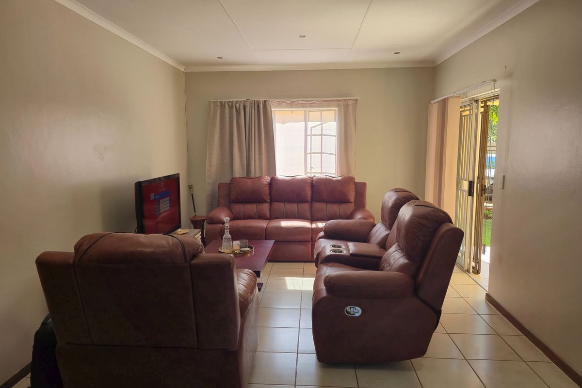 A spacious living room featuring tiled flooring, recessed downlighting, and a sliding glass door providing access to the outdoor area.