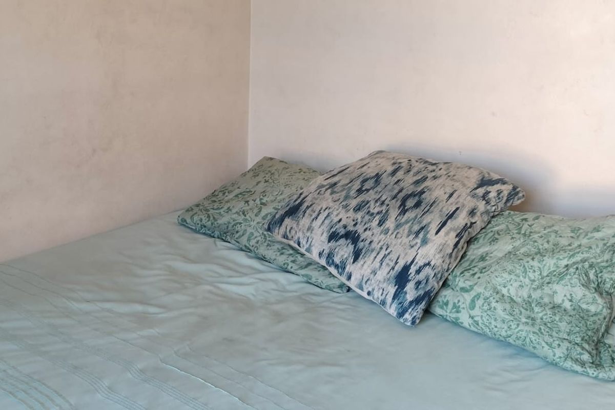 A corner view of a bedroom featuring plain walls and a bed setup.