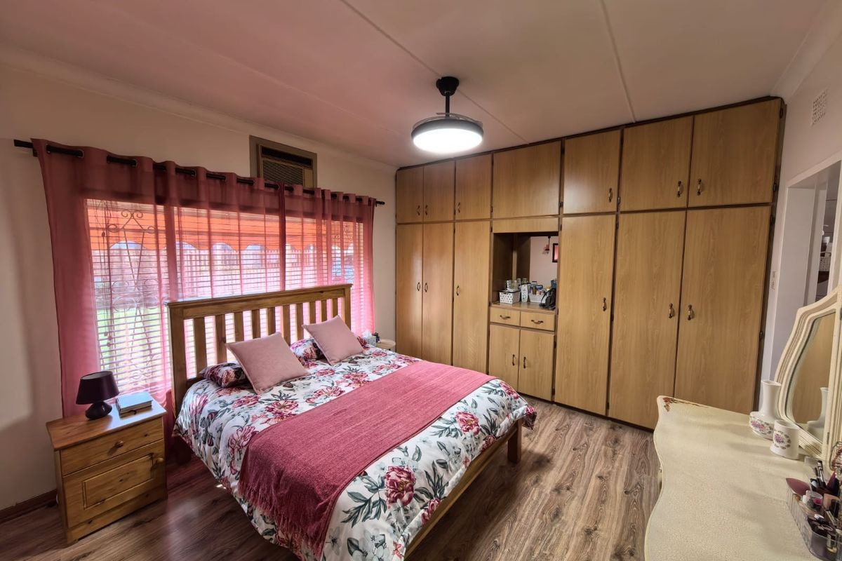 A bedroom featuring extensive built-in wooden cabinetry, wood-look flooring, and a window with integrated security bars.