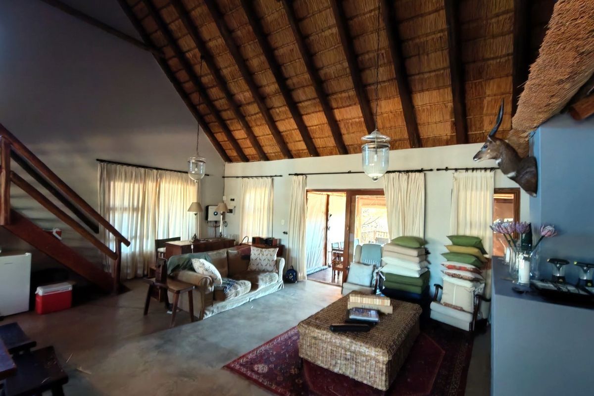 Spacious living area featuring a high vaulted thatched ceiling, exposed timber beams, concrete flooring, and a staircase leading to an upper level.