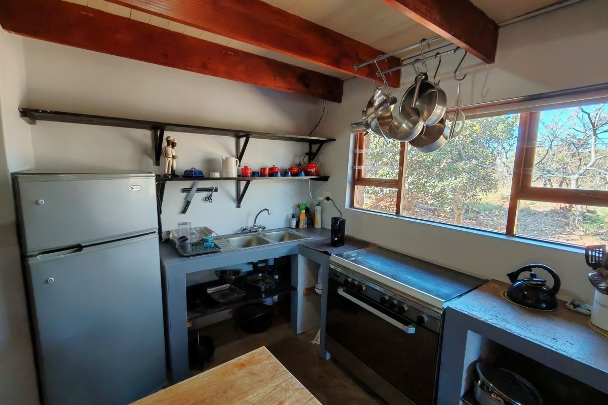 Rustic kitchen featuring exposed timber ceiling beams, concrete-style cabinetry, double sink, and a built-in oven with cooktop, overlooking a natural garden setting.