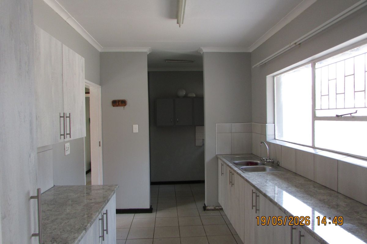 A functional kitchen featuring light-toned cabinetry, granite-look countertops, a double stainless steel sink, and tiled flooring with a connected scullery area.