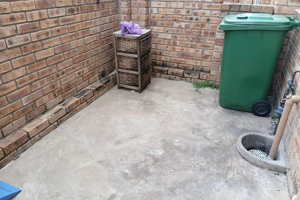A small, utilitarian outdoor courtyard area featuring exposed brick walls, concrete flooring, and integrated drainage infrastructure.