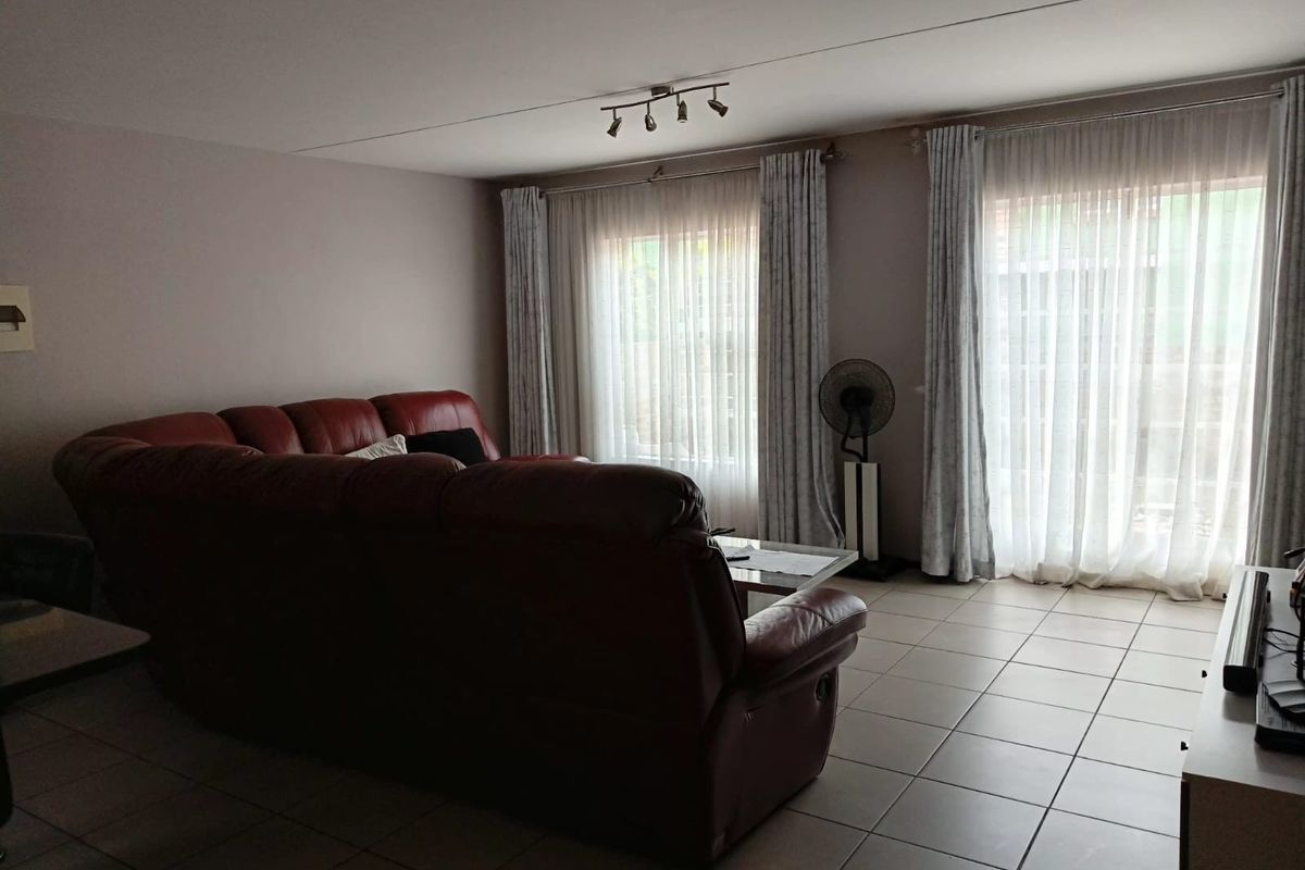 A spacious living room featuring neutral tiled flooring and large windows with floor-to-ceiling curtains, providing ample natural light and access to the exterior.
