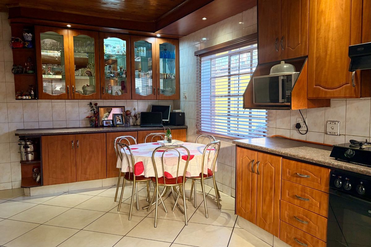 A functional kitchen featuring wooden cabinetry, tiled flooring, and a built-in oven and hob, with an integrated dining area.
