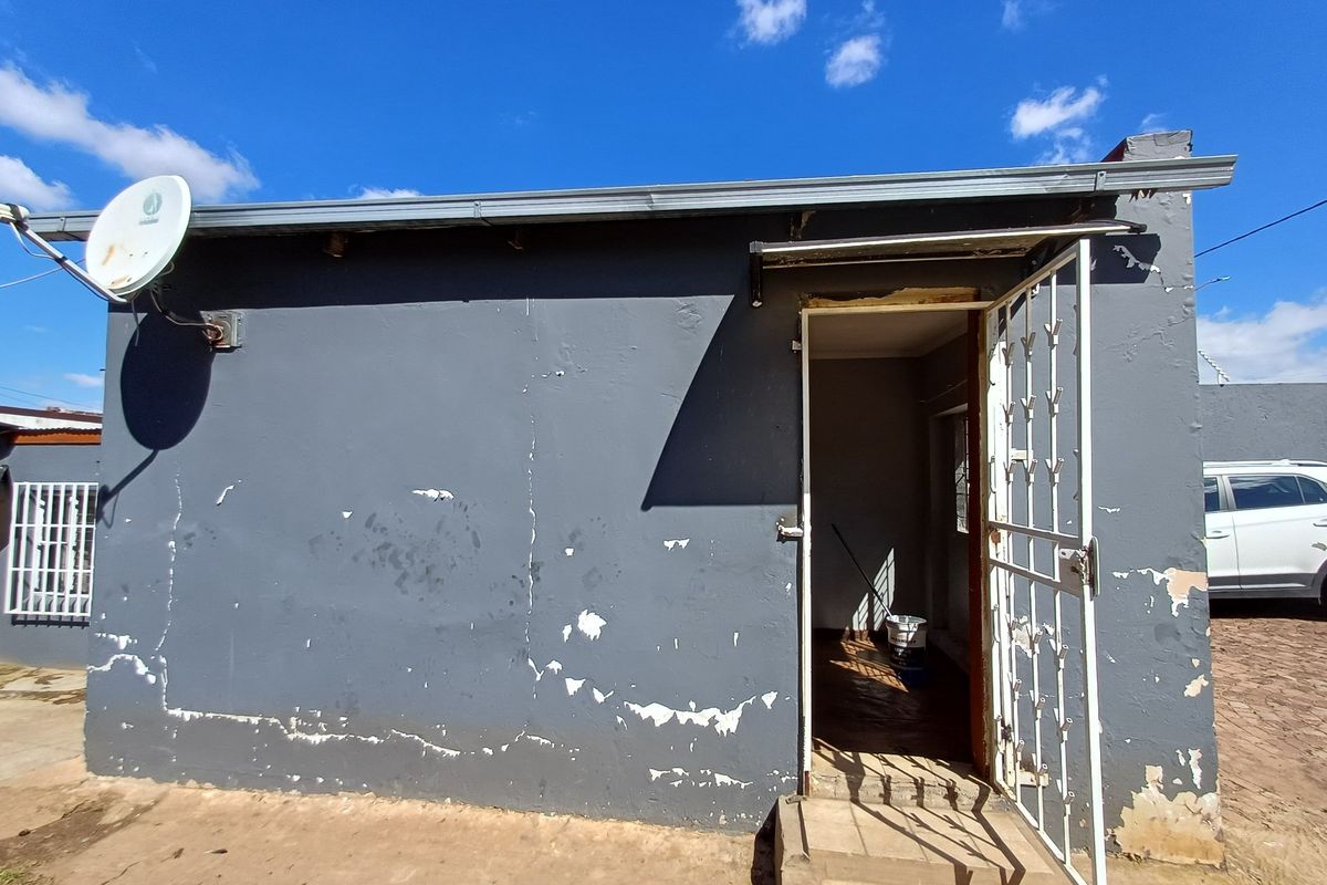 Exterior view of a small outbuilding featuring a security gate, satellite dish, and worn exterior wall finishes requiring maintenance.