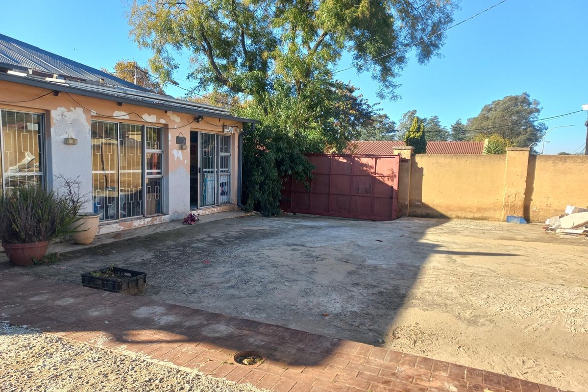 Rear exterior view of the property featuring a large paved courtyard, perimeter boundary wall, and sliding glass doors with security gates.