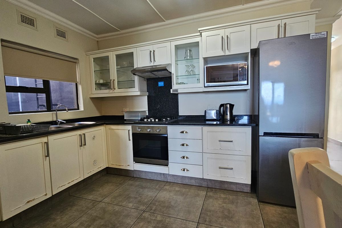 A functional kitchen featuring white cabinetry, dark granite countertops, a built-in oven, hob, and extractor fan, with tiled flooring throughout.