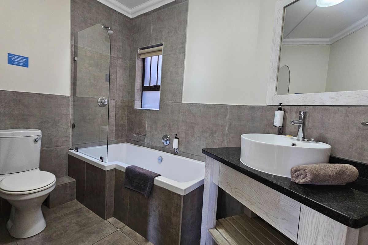 Modern bathroom featuring a contemporary vanity with a vessel sink, a bathtub with a glass shower screen, and neutral grey wall and floor tiling.