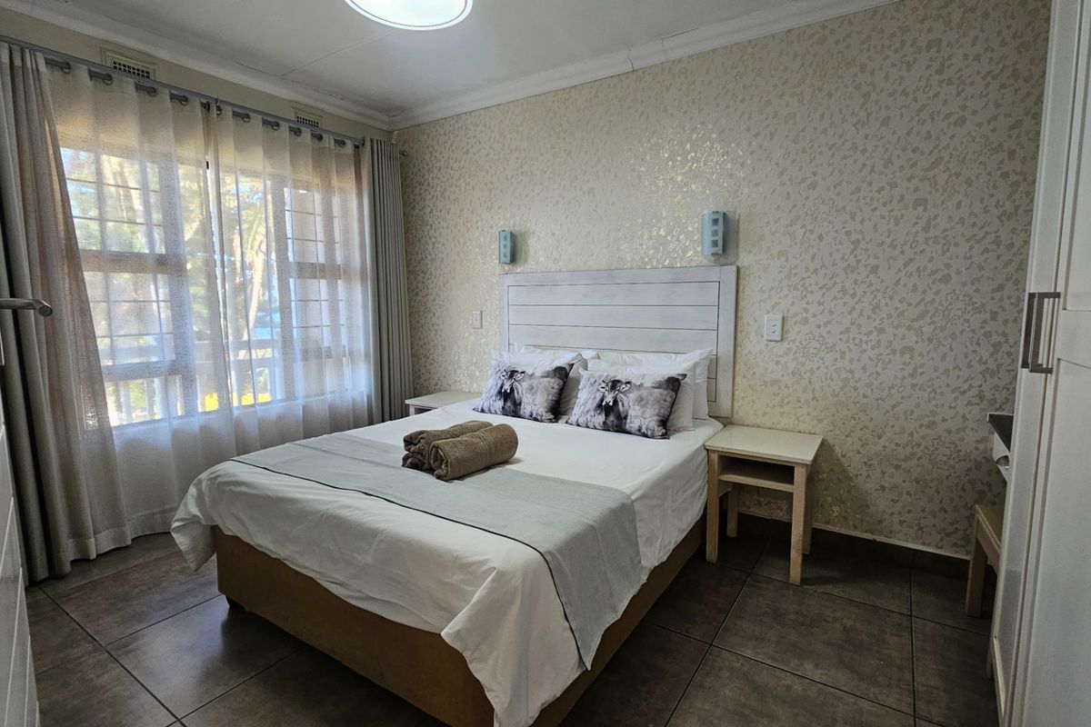A well-maintained bedroom featuring tiled flooring, textured wallpaper, built-in headboard, and large windows with curtains.