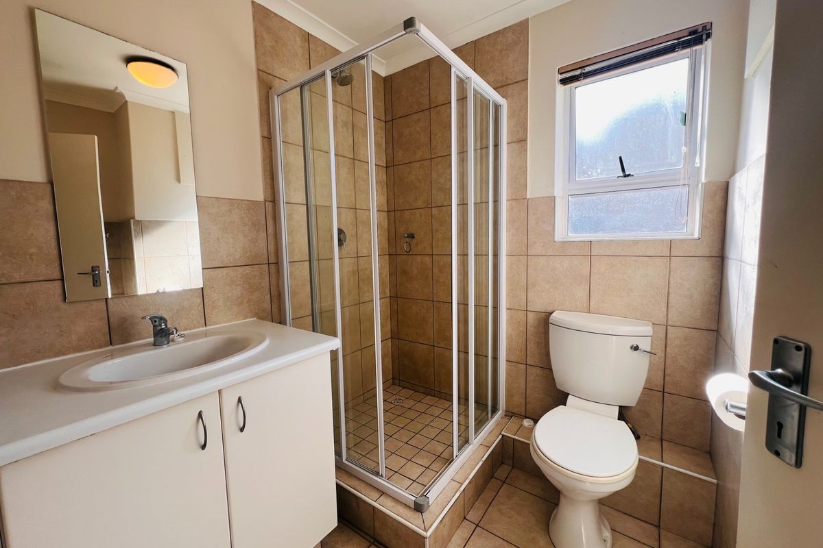 A functional bathroom featuring a corner shower enclosure, vanity cabinet with integrated basin, and a standard toilet with tiled walls and flooring.