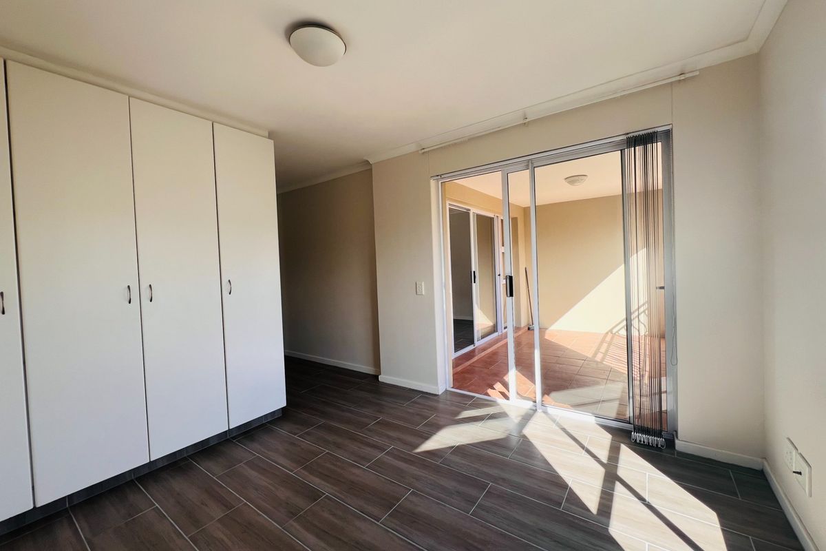 A bright bedroom featuring modern wood-look tile flooring, built-in wardrobes, and sliding glass doors that open onto a private balcony.